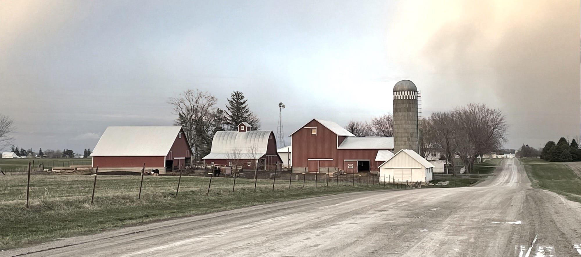 a dirt road leading to a farm with a barn and silo in the background