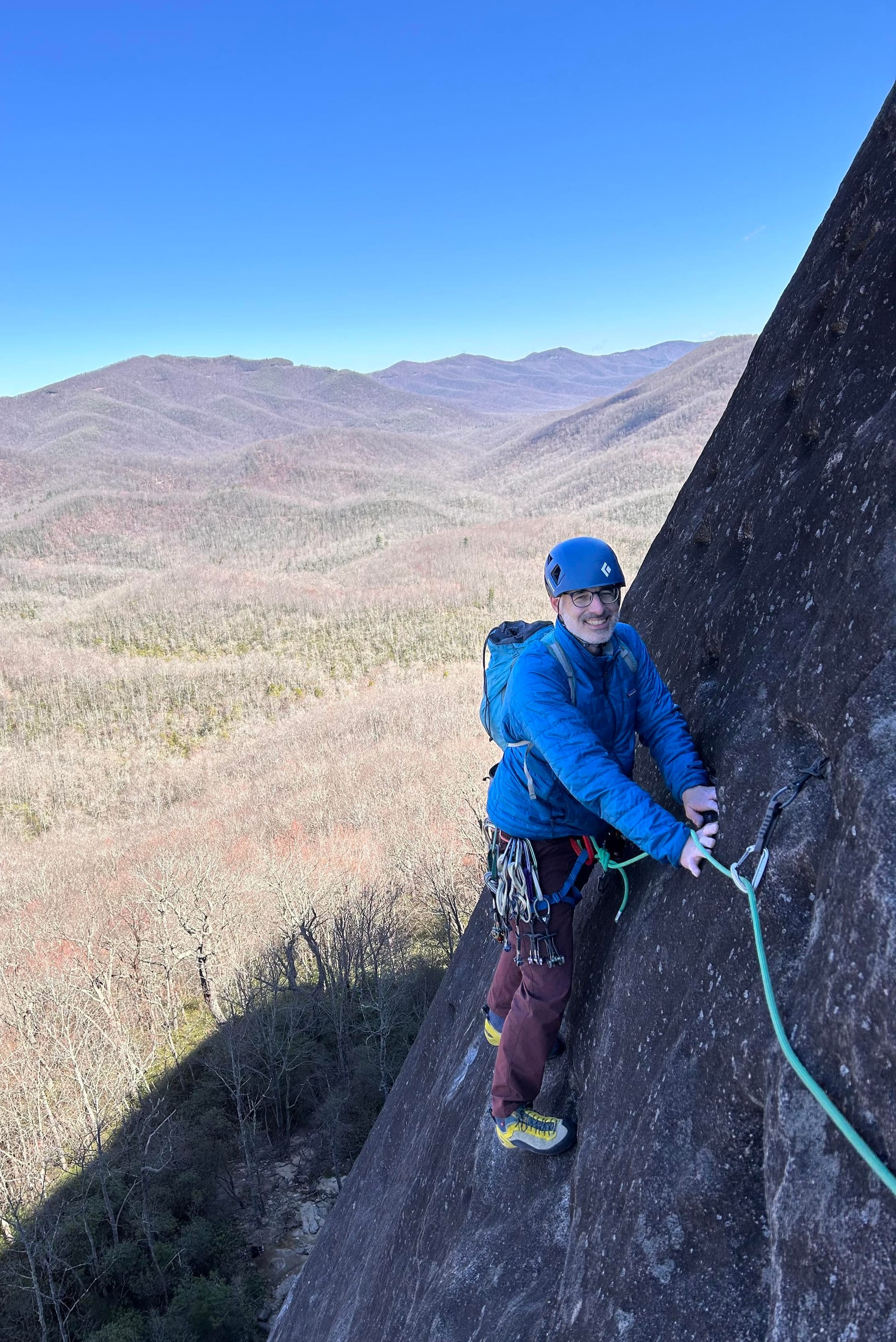 me standing on a cliff attached to a rope with forested mountains in background