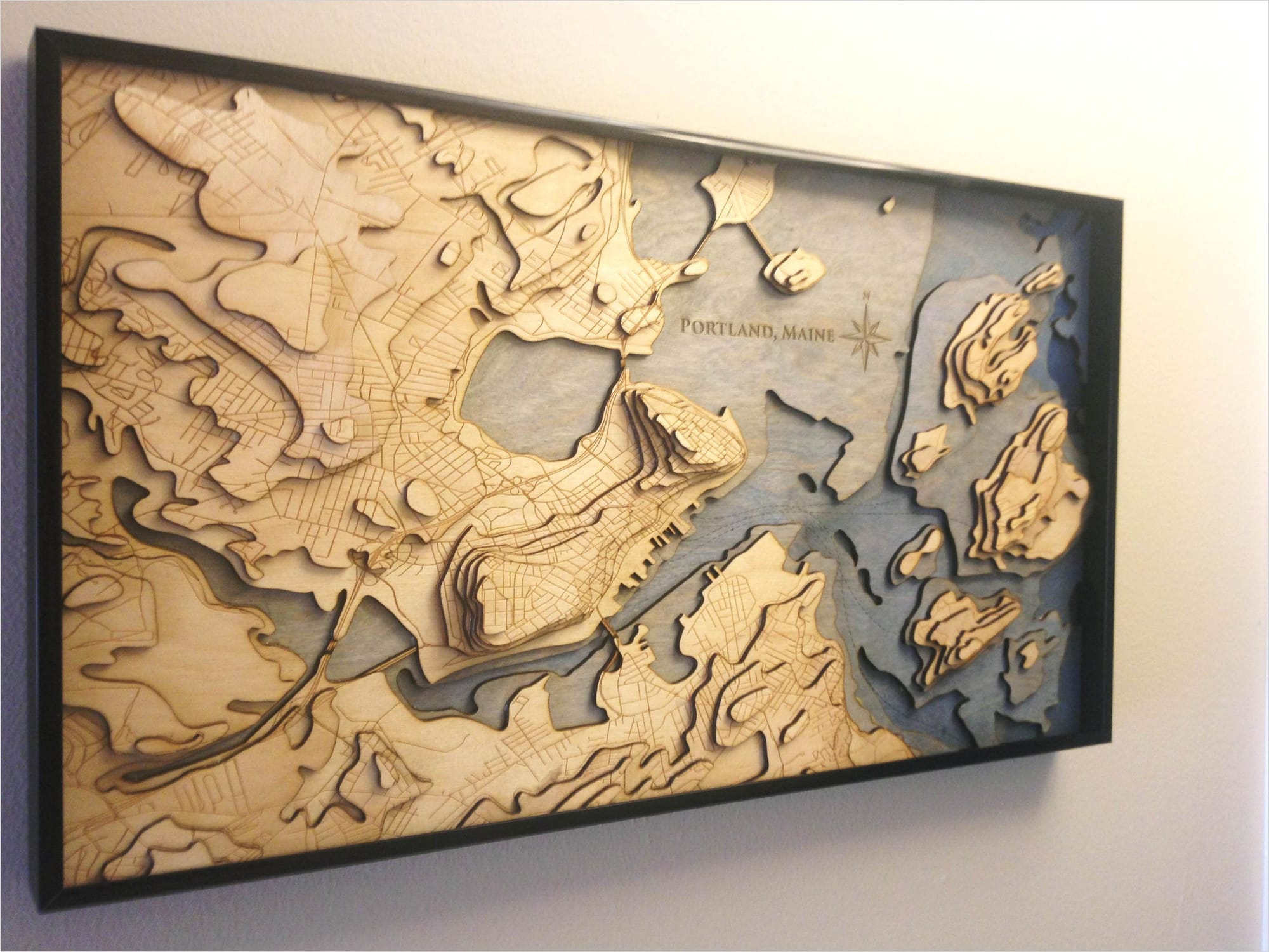 framed wooden topographic map of Portland, Maine, hanging on a wall