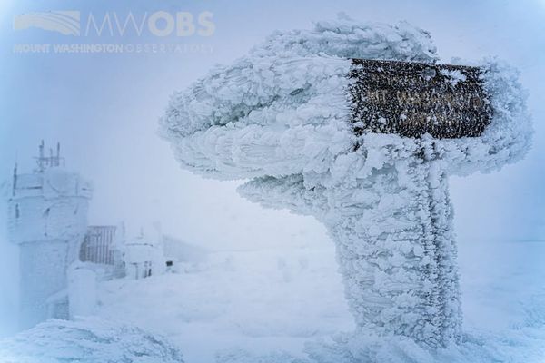 sign reading "Mt Washington summit", covered in ice that's frozen in a sideways orientation from strong winds
