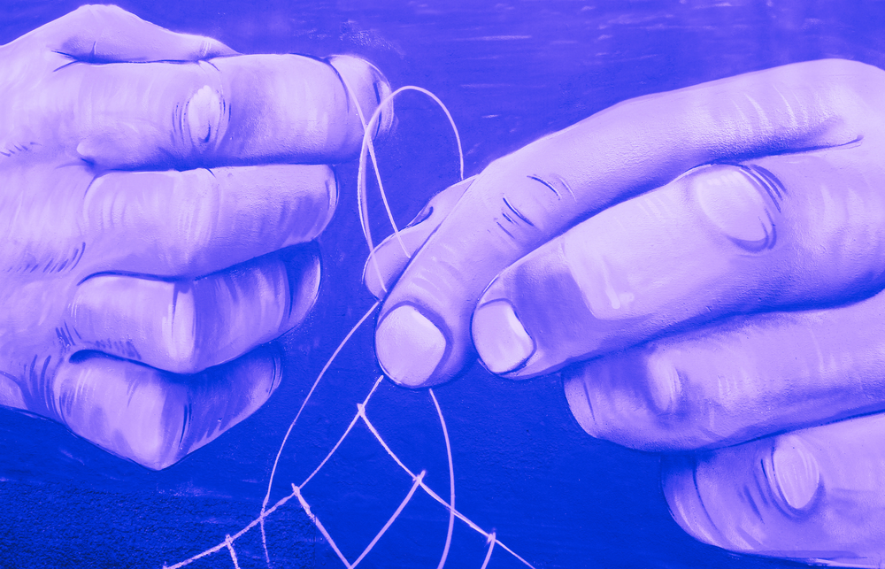 A close up of hands tying thread into a web. 