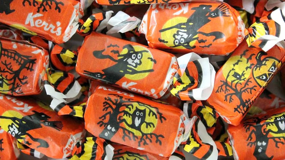 Kerr's Molasses candy wrapped in orange,  yellow, and black halloween wrappers, adorned in images. of witches, jack-o-lanterns and owls in bare-branched trees. 