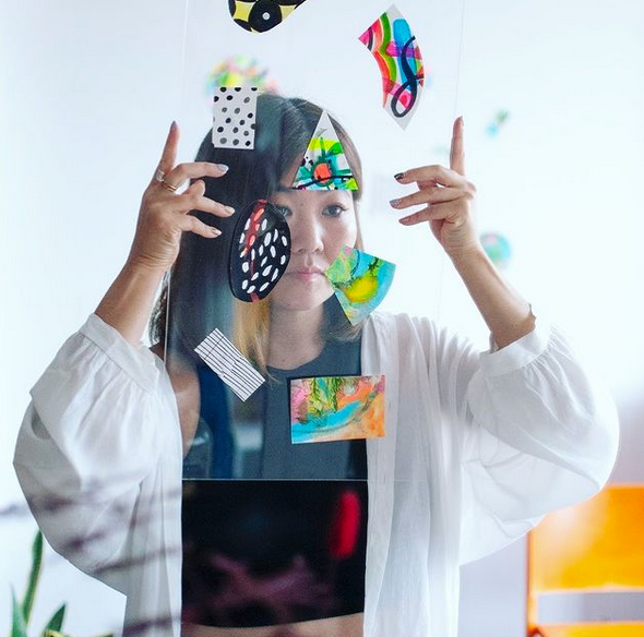 emmie in studio behind a clear plastic square with coloured shapes. emiie's face is visible through the panel, but obscured b