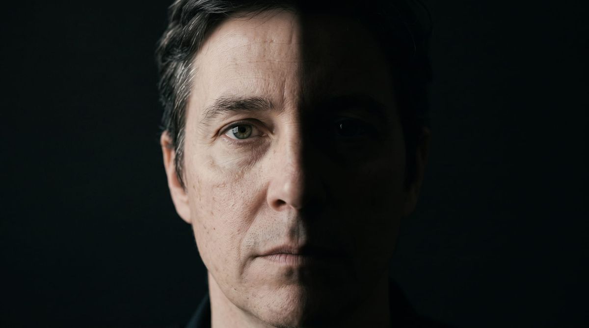 Editorial portrait of a face split cleanly down the center by light and shadow, representing internal psychological conflict and cognitive dissonance.