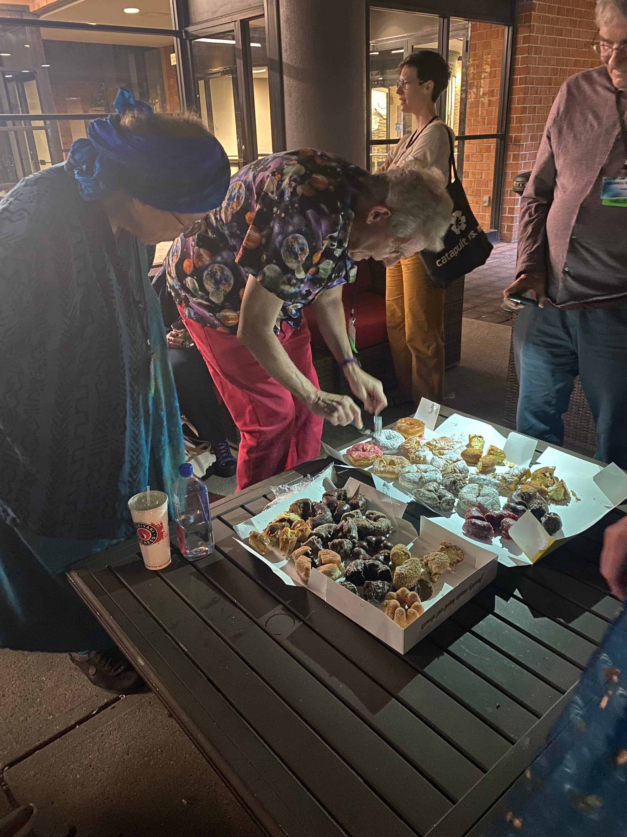 Scott Edelman cuts up donuts to share with Readercon attendees while Greer Gilman surpervises. 