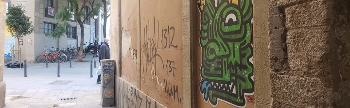 Graffito of a stylized green monster on a wall in a European-looking city.