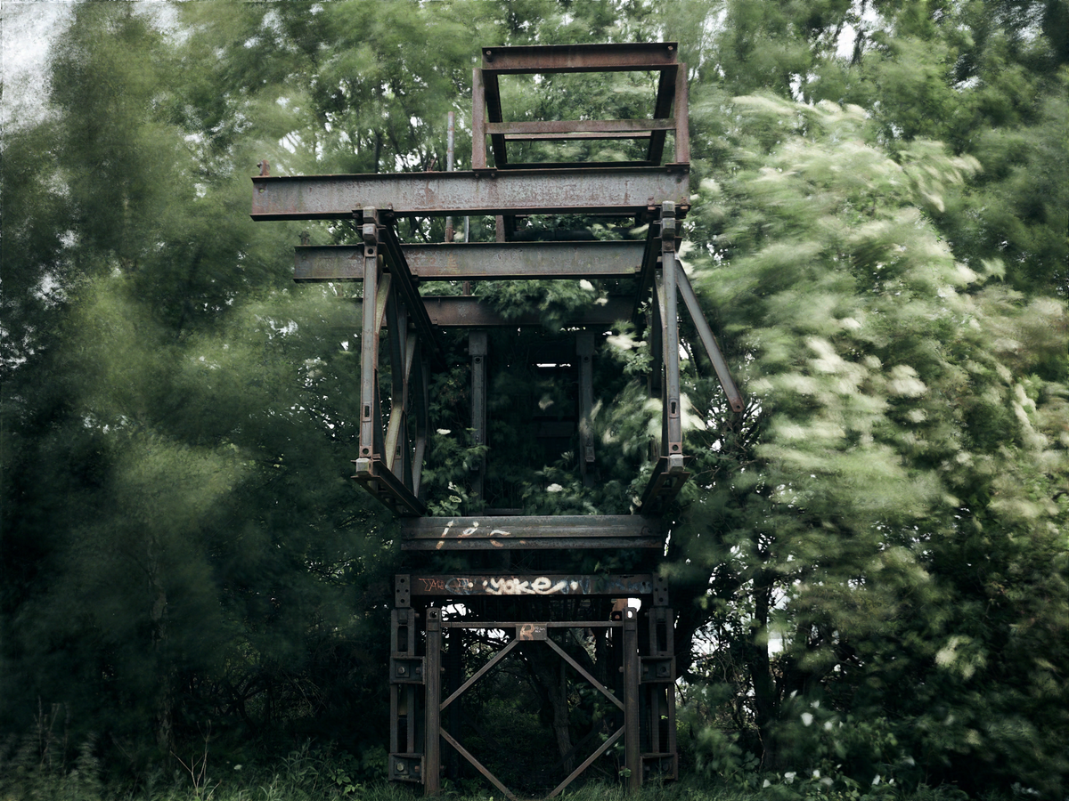 Disused, rusting conveyor belt structure surrounded by foliage blurred by movement in the wind.