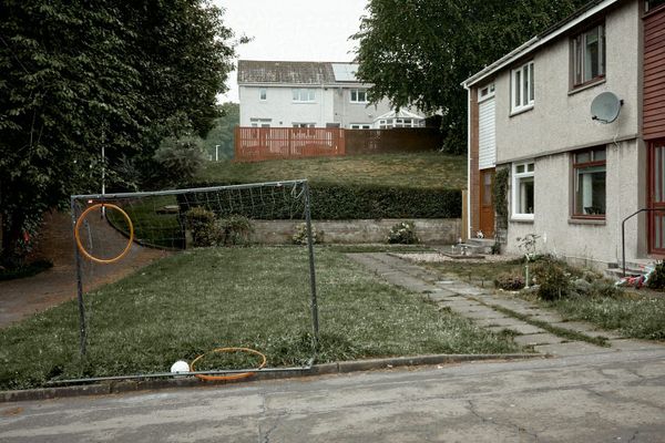 A colour image of a child's football goal in a garden of a suburban house, surrounded by trees and other houses.