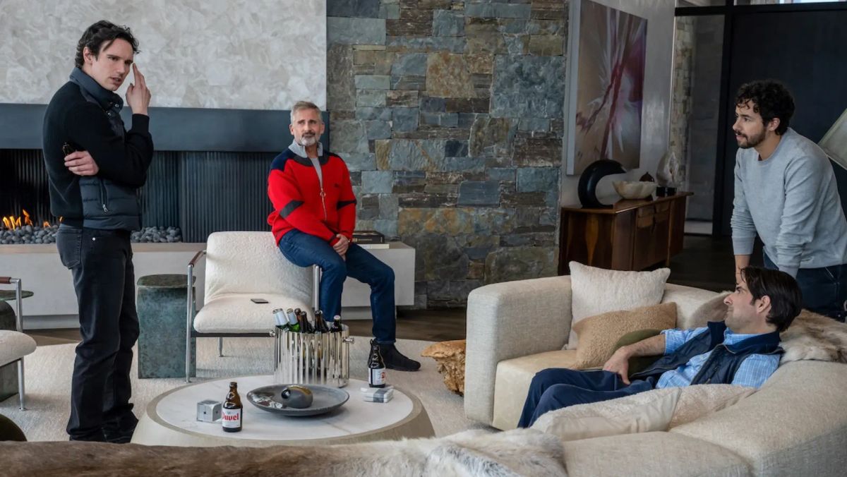 Four men in a modern living room with stone walls and fireplace, drinking beer, one standing, one on chair arm, two on sofa.