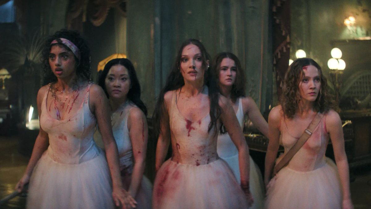 Five young women in blood-stained white ballet dresses stand together in a dimly lit ornate room, looking tense and alert.