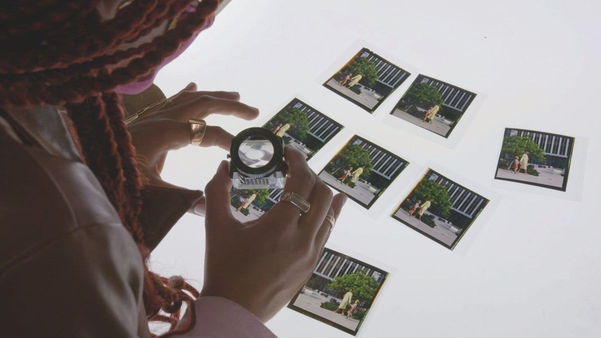 Person with red braids examines printed photographs on a white surface using a photographer's loupe magnifier.
