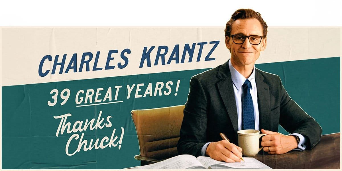 Man in suit and glasses at desk with book and coffee mug, beside banner reading "Charles Krantz 39 Great Years! Thanks Chuck!"