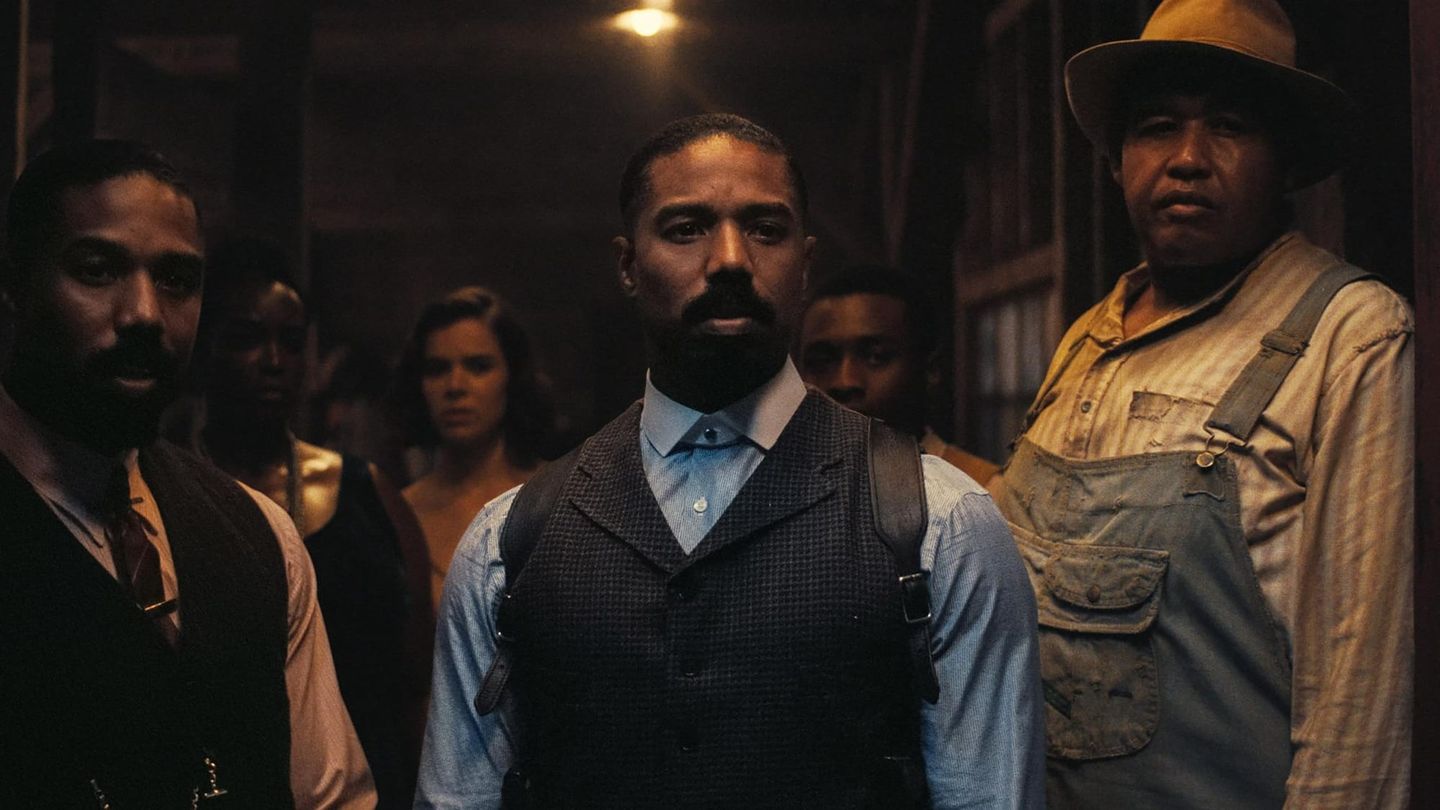 Three men stand in a dimly lit room; the center man wears a vest, blue shirt, and holster, flanked by others in period clothing.