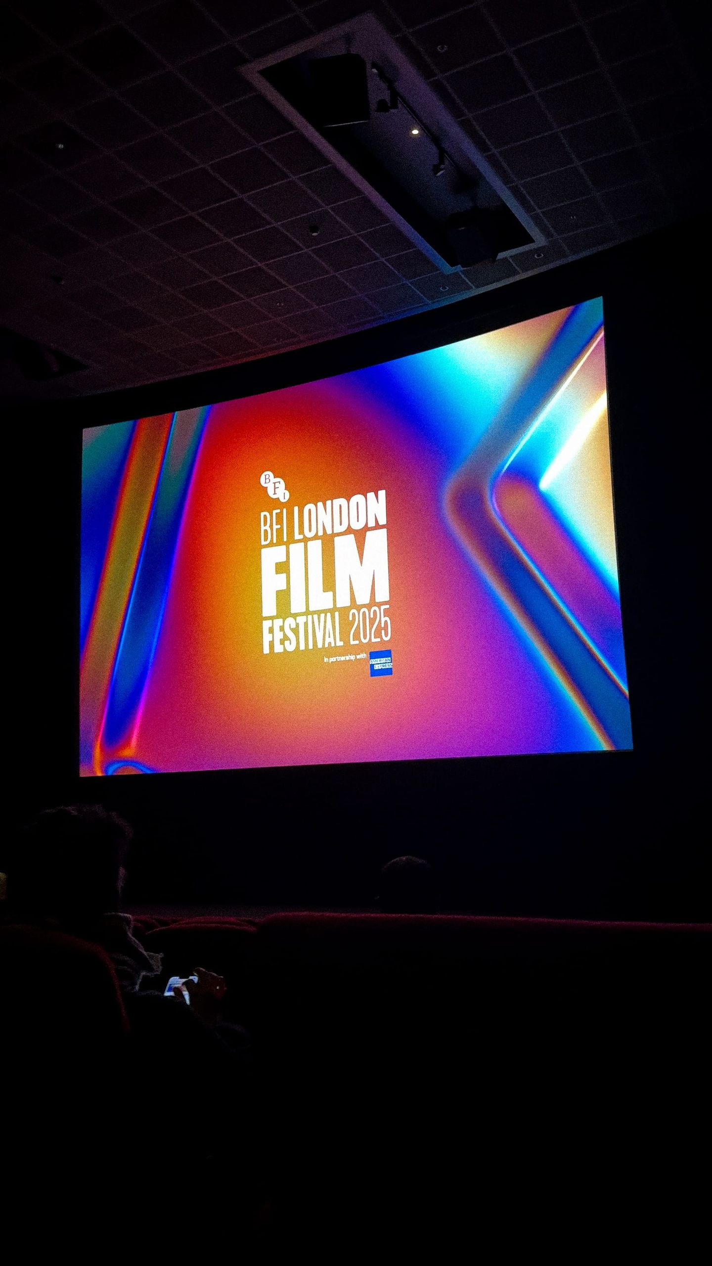 Cinema screen displaying "BFI London Film Festival 2025" logo on a colorful gradient background, seen from dark auditorium seats.