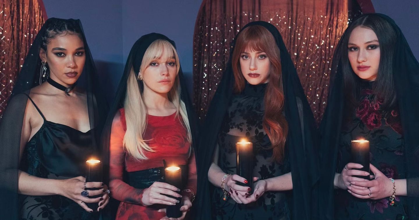 Four women in dark veils holding lit candles, wearing gothic-style clothing against sparkly red curtains in moody lighting.