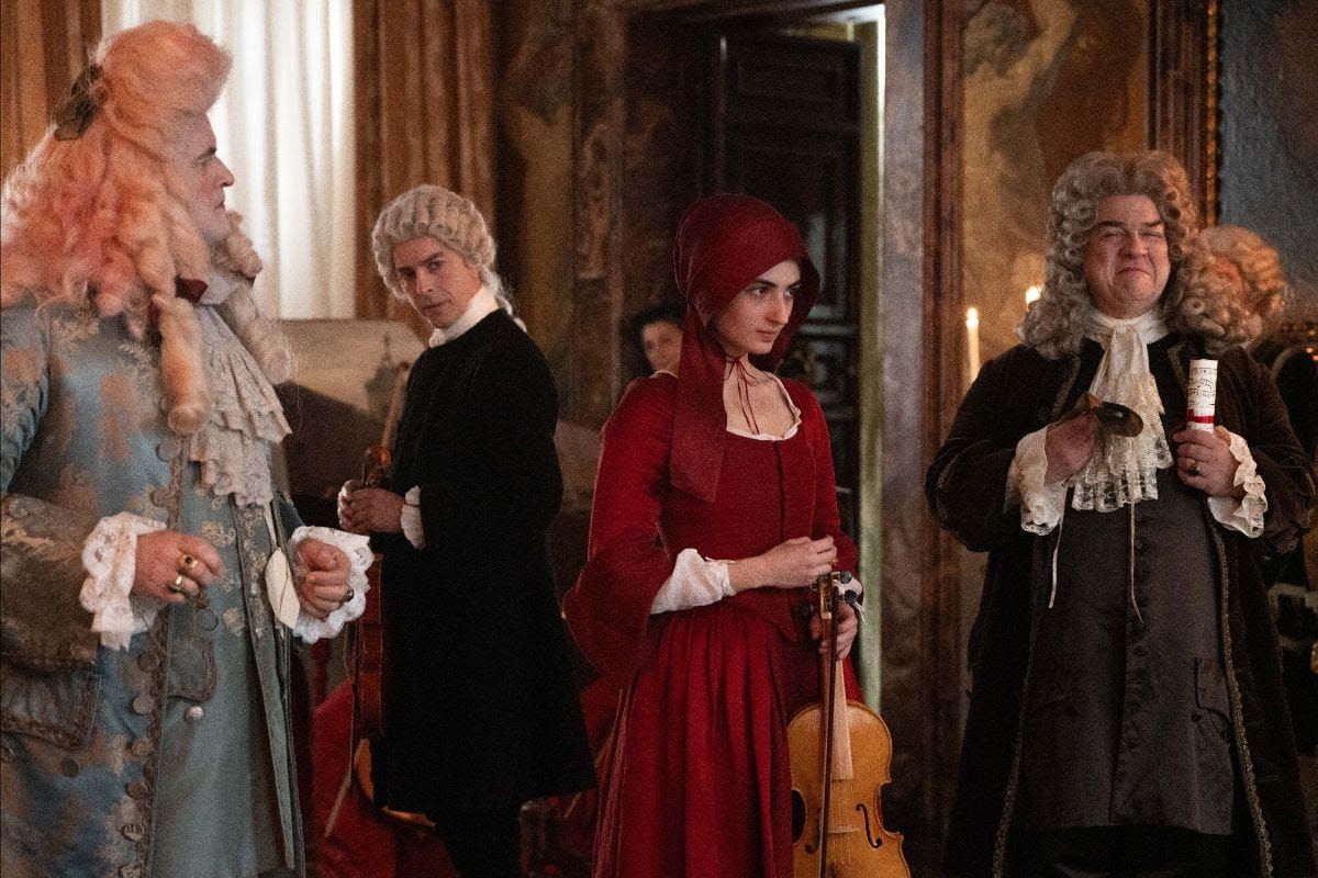 Four people in 18th-century Baroque costumes with powdered wigs and lace; center figure in red dress holds a violin.