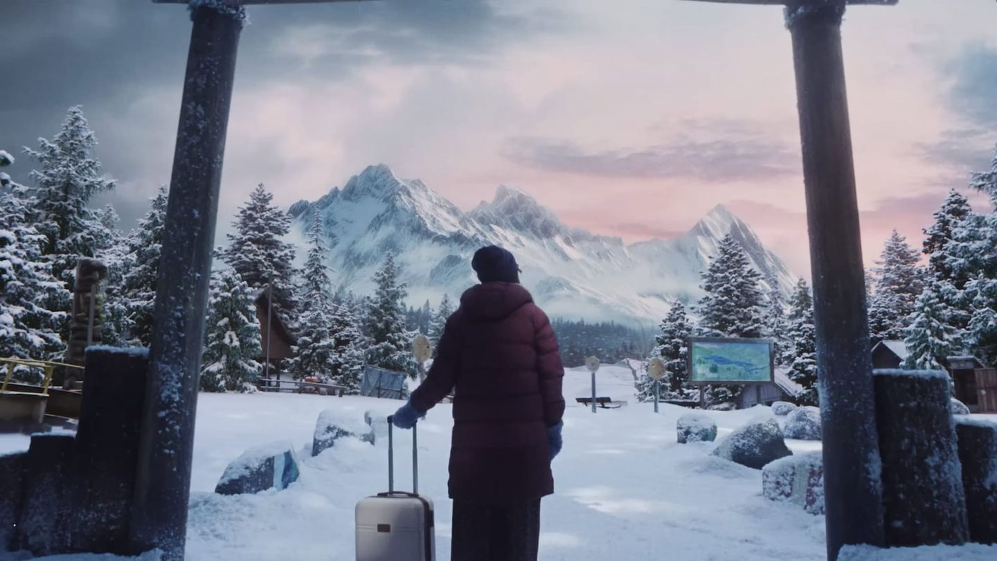 A lone figure with luggage arrives at a snowy Camp Miasma entrance, with cabins, pine trees and mountains beyond the gate.