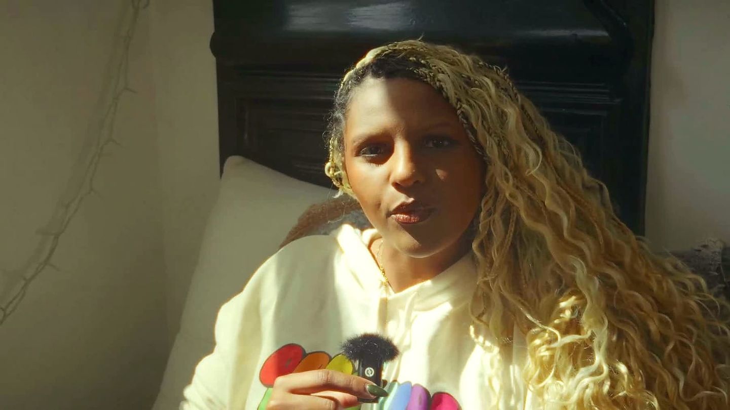 Umnia in a white hoodie holding a small microphone in a warm still from Thought Summer.