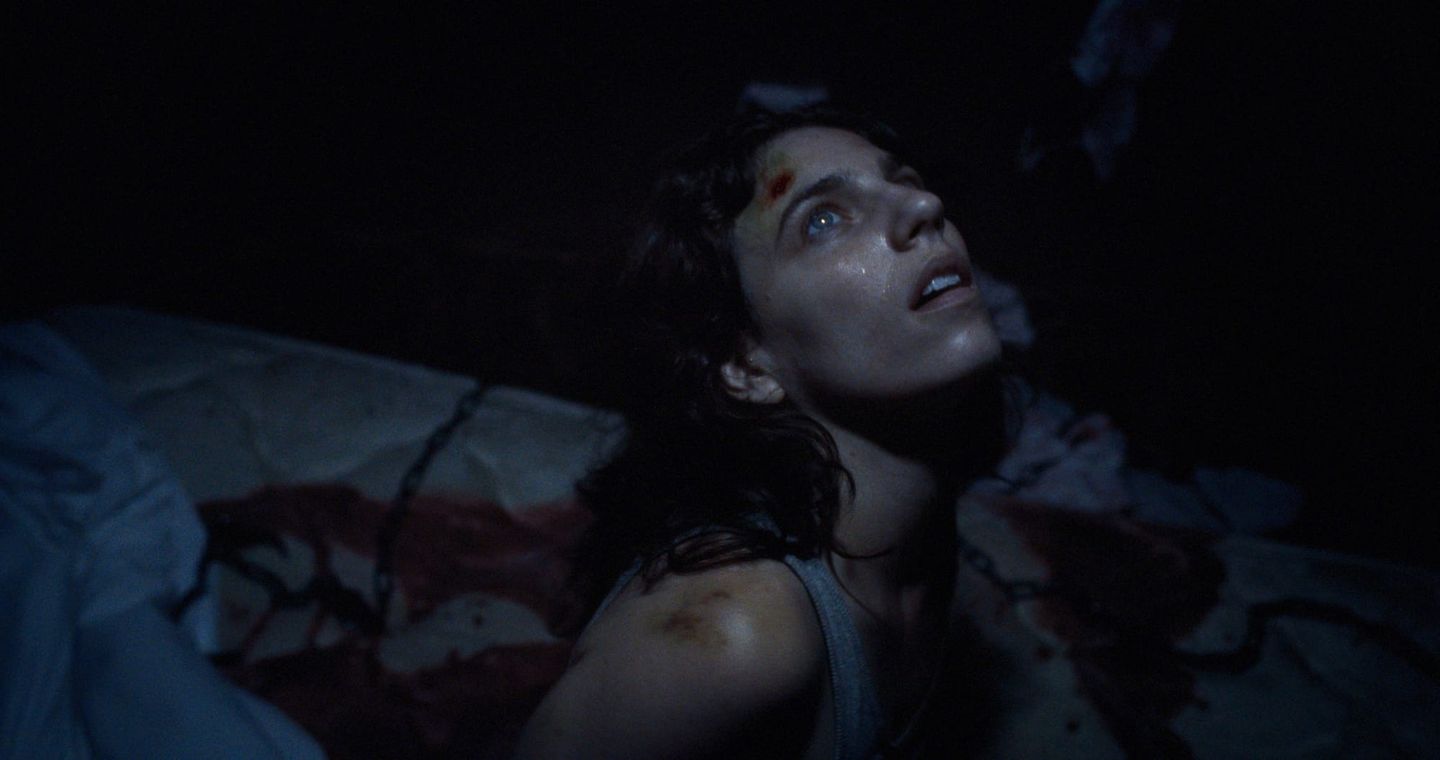A frightened injured woman lying in a dark room in Hellcat.
