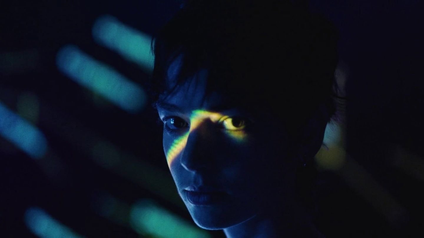 Close-up of a person’s face in darkness with blue and green light projected across their eyes.