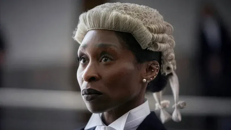 Close-up of Cynthia Erivo in a barrister’s wig and dark court attire, with a courtroom blurred behind her.