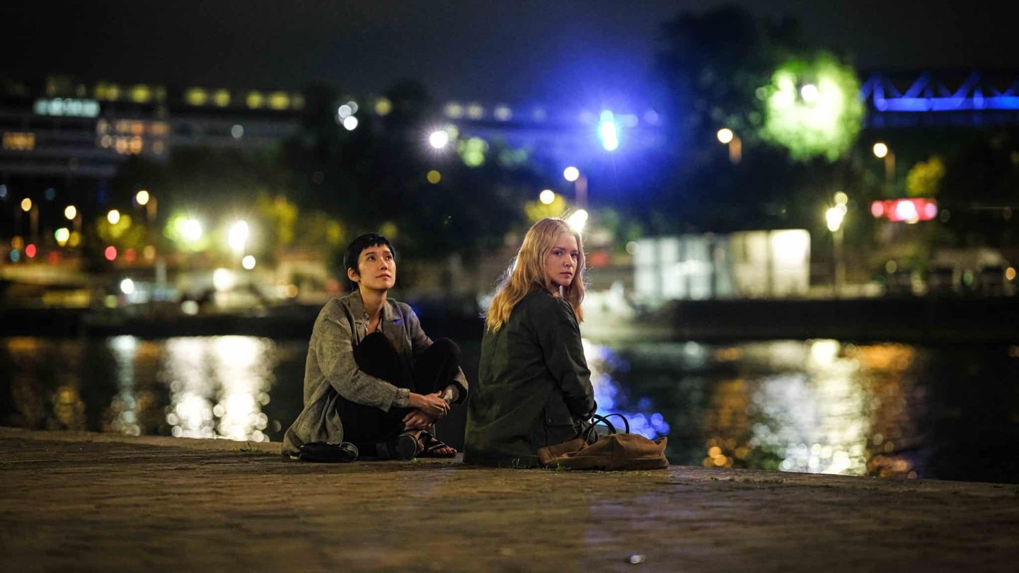 Tao Okamoto as Mari Morisaki and Virginie Efira as Marie-Lou Fontaine sit by a river at night in All of a Sudden.