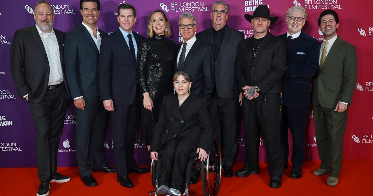 Ten people pose on a red carpet in front of a BFI London Film Festival backdrop; one woman in a black suit sits in a wheelchair.