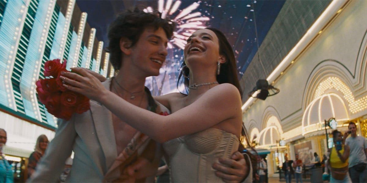 Young couple embracing and laughing on the Las Vegas Fremont Street Experience, she holds red roses, fireworks on LED ceiling above.