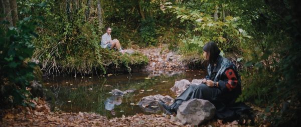 Two teenage girls, Ceren and Azra, sit across from each other at a verdant pond.