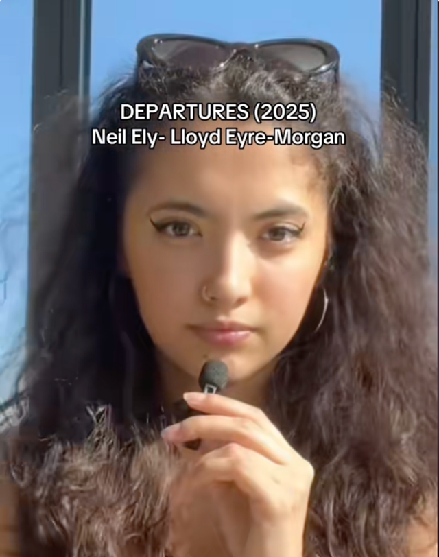 Young woman with curly dark hair, sunglasses on head, holding a small microphone. Text reads "DEPARTURES (2025) Neil Ely- Lloyd Eyre-Morgan"