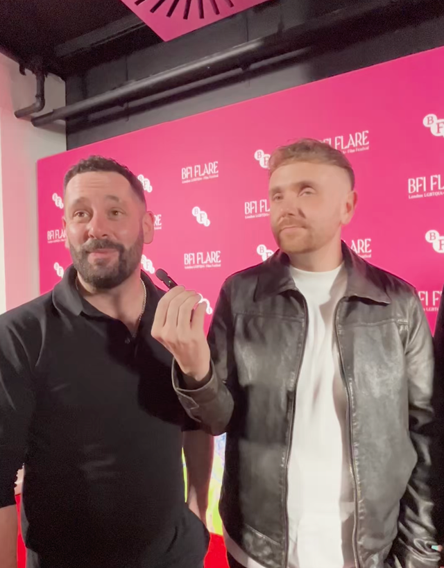 Two men posing at BFI Flare London LGBTIQ+ Film Festival, one in black polo, other in leather jacket over white tee.