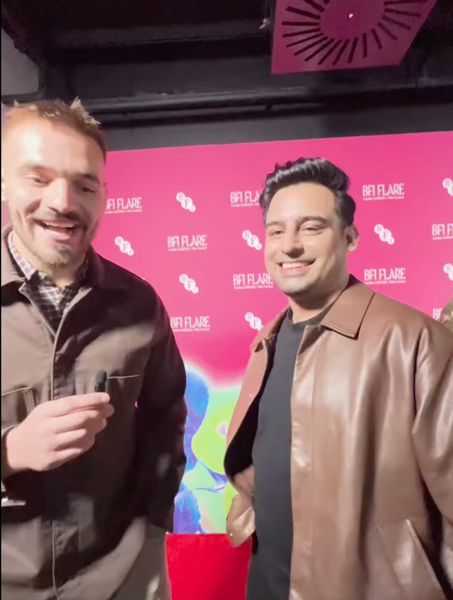 Two smiling men posing at a BFI Flare film festival event against a pink branded backdrop, both wearing brown jackets.
