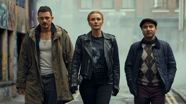 Three people walk toward the camera down a foggy urban alley with graffiti walls, wearing jackets in a cinematic style.