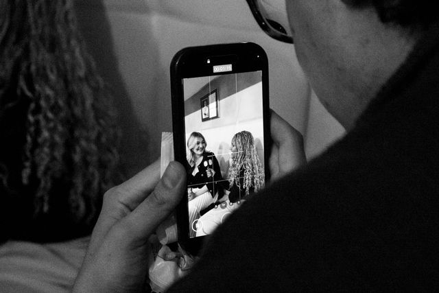 Someone recording two smiling women on a smartphone, one with straight hair and one with curly hair, in black and white.