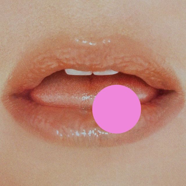 Close-up of slightly parted glossy lips with visible front teeth, partially obscured by a pink circle graphic overlay.