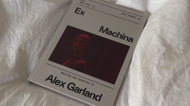 Book cover of "Ex Machina" by Alex Garland, published by A24, Book Number 001, with a red-tinted photo of a figure, on white bedsheets.
