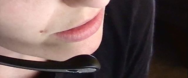 Close-up of a person's lower face with a slight smile, wearing a black headset microphone near their chin.