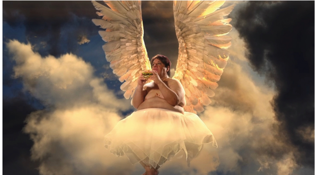 Shirtless man with large angel wings and white tutu eating a burger while floating among dramatic clouds in golden light.