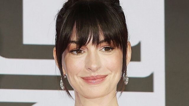 Smiling woman with dark hair in an updo with bangs, wearing sparkly drop earrings, at a media event.