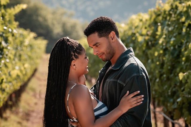 Couple embracing and gazing at each other lovingly between rows of grapevines in a sunlit vineyard.