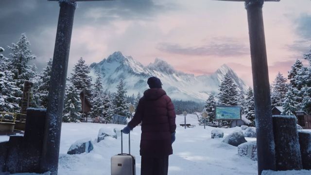 A lone figure with luggage arrives at a snowy Camp Miasma entrance, with cabins, pine trees and mountains beyond the gate.