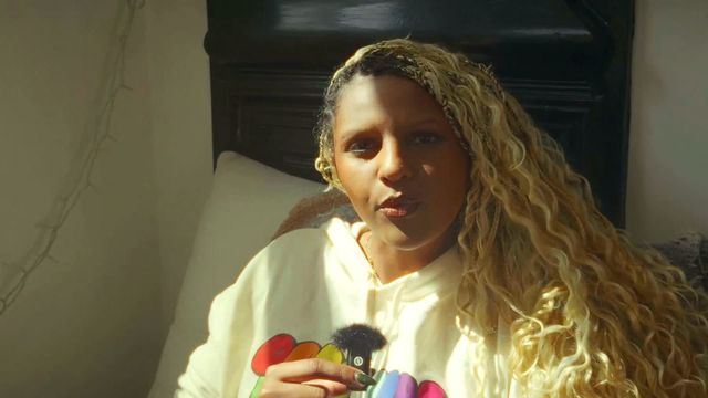 Umnia in a white hoodie holding a small microphone in a warm still from Thought Summer.