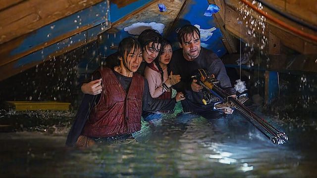 Four people sheltering in floodwater beneath a structure, one holding a spear gun, in The Last House.