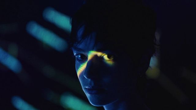 Close-up of a person’s face in darkness with blue and green light projected across their eyes.