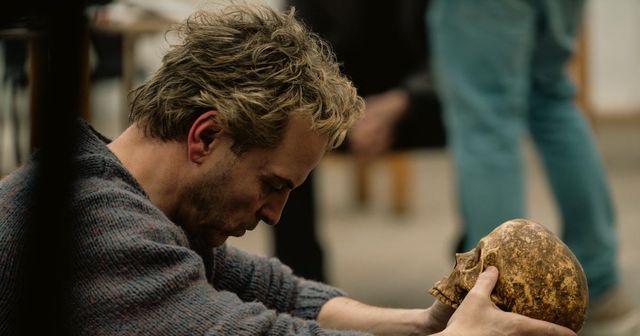 Andrew Scott as Ian Charleson holds a skull while leaning forward in a muted rehearsal-room scene from Elsinore.