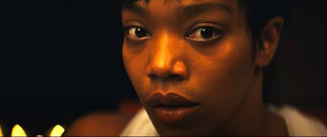 Close-up of a young person's face lit by warm firelight, eyes wide with an expression of concern or fear, dark background.