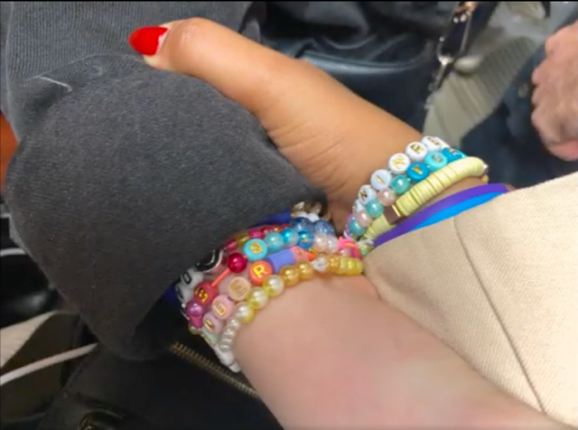 Close-up of a hand with red nail polish wearing multiple colorful beaded friendship bracelets with letter beads on the wrist.