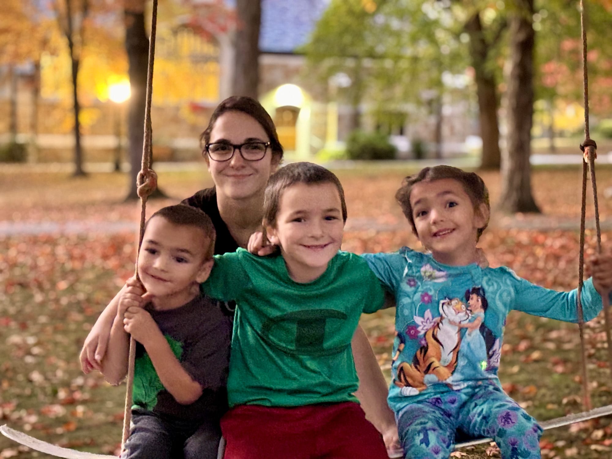 A mother with her three young children sitting on a swing surrounded by autumn trees at Bates College in Lewiston, Maine.