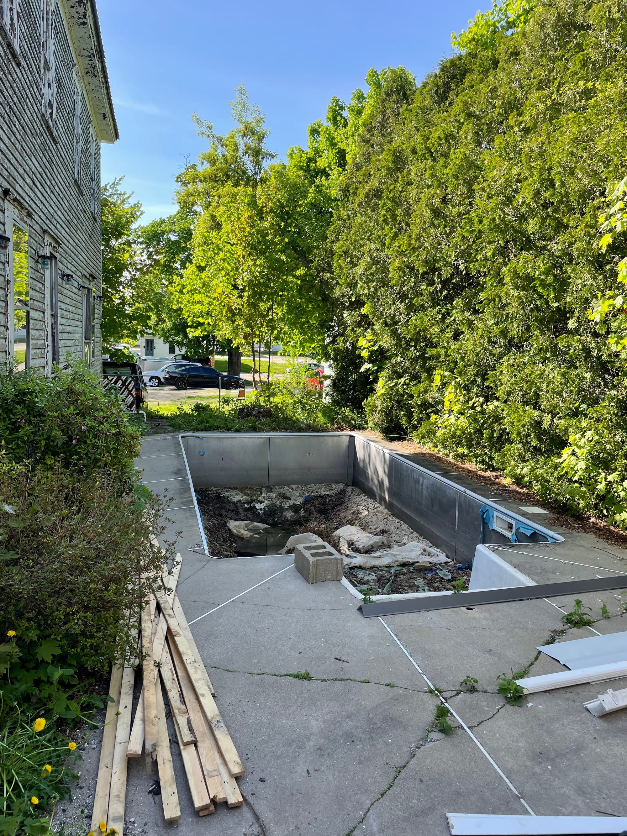 Old in-ground pool in disrepair, surrounded by cracked concrete and overgrown edges