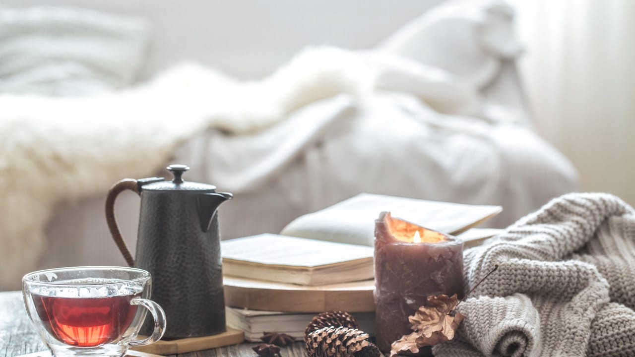 A warm and inviting indoor scene with a steaming cup of tea, an open book, and a soft blanket, perfect for relaxation.